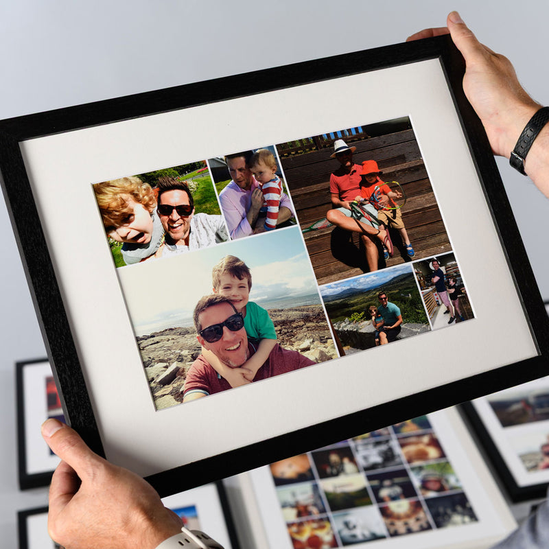 A person holds a black-framed matted photo collage print featuring multiple family photographs. The frame is shown at an angle with hands holding it, and other framed prints are visible in the background.